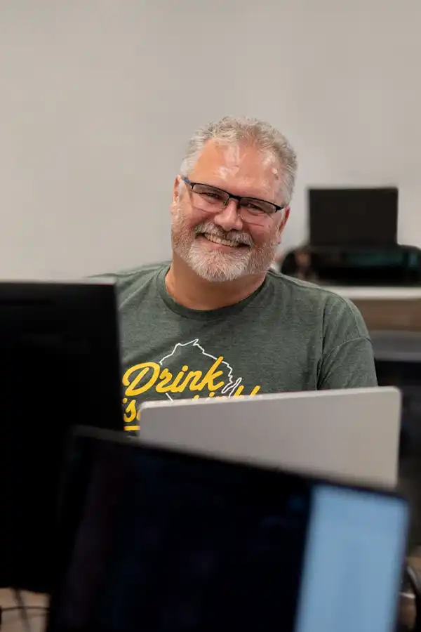 A man with a majestic beard sitting behind a laptop and smiling at the camera. A man with a majestic beard sitting behind a laptop and smiling at the camera.